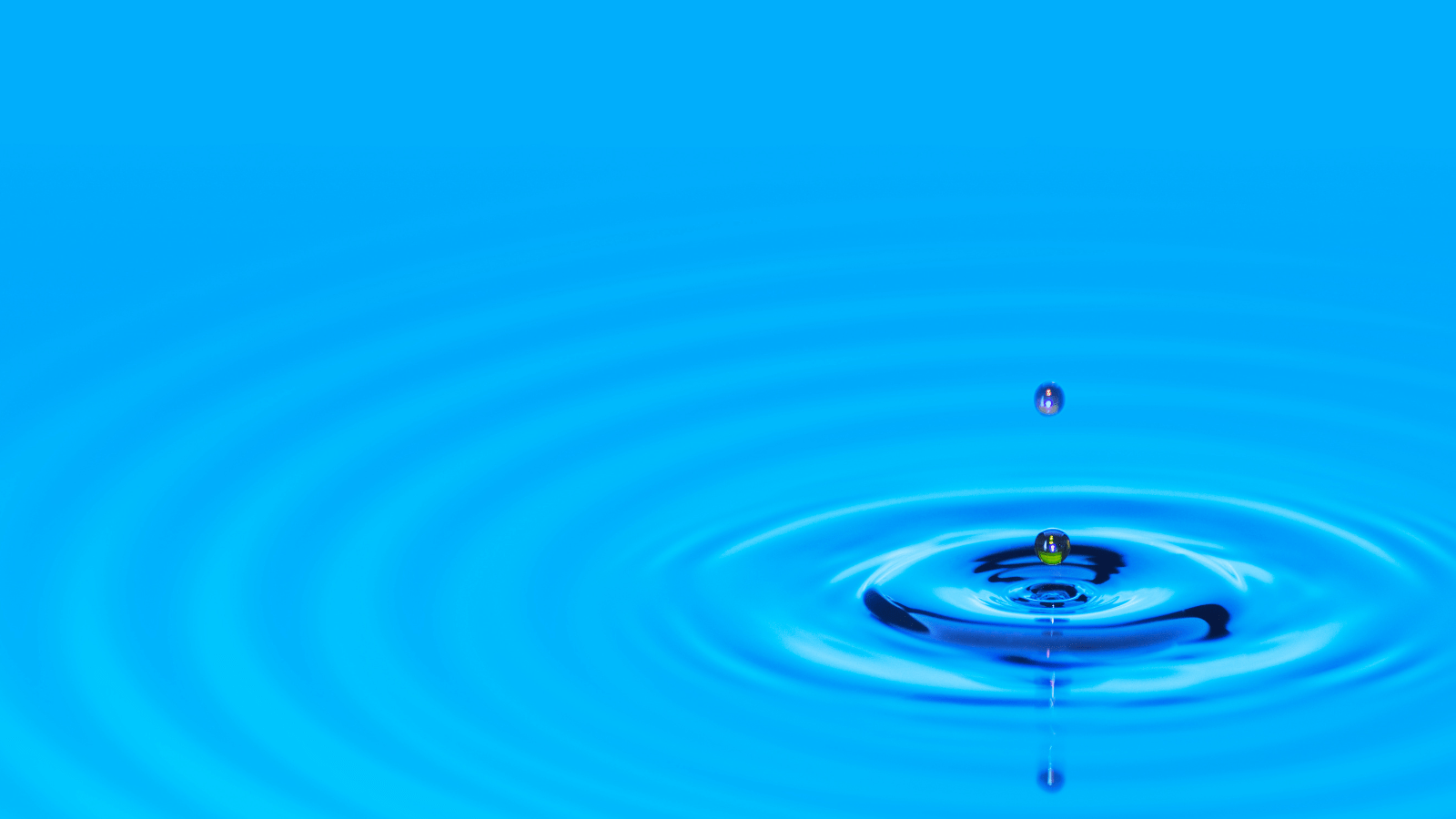 a droplet of water creating a ripple on a blue body of water
